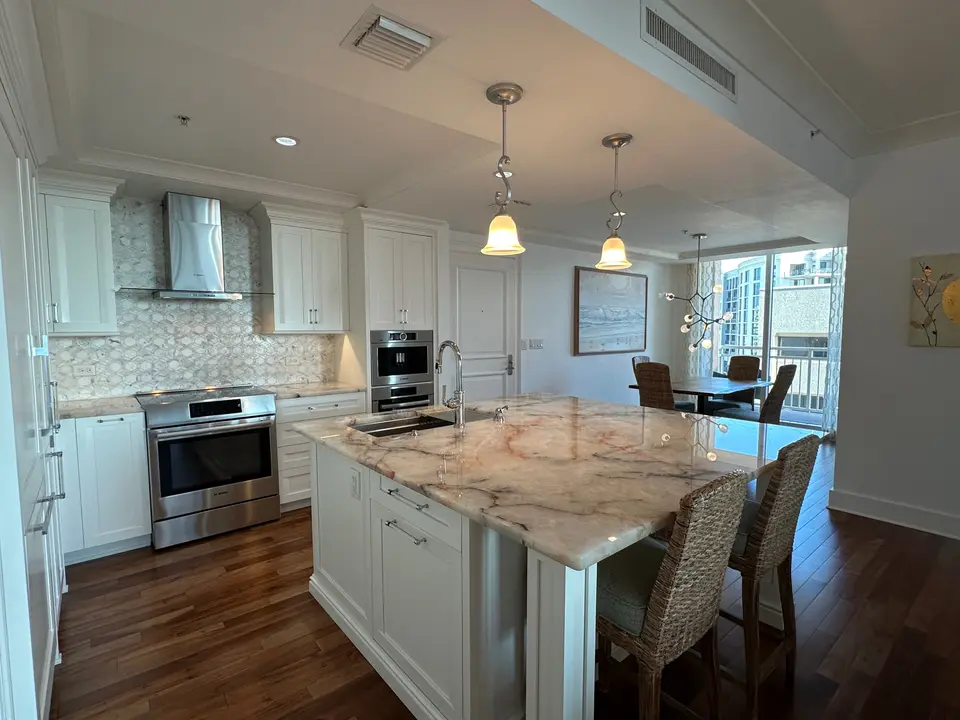 Open kitchen with marble island, white cabinetry, wood floors and stainless appliances