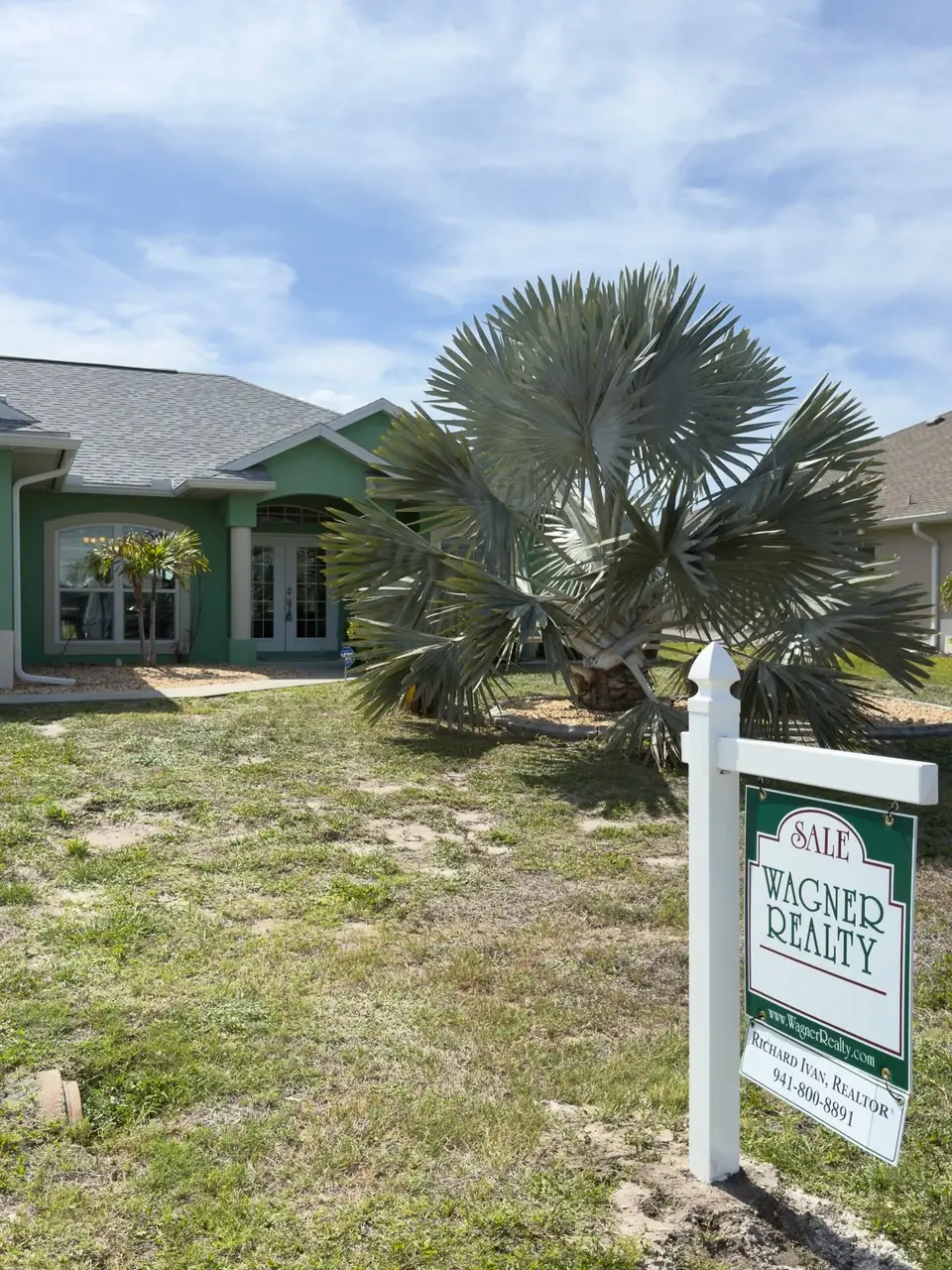 Front yard with a Wagner Realty sale sign and palm