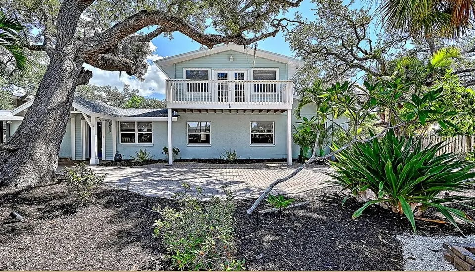 Two-story Siesta Key home under oaks with a fenced yard