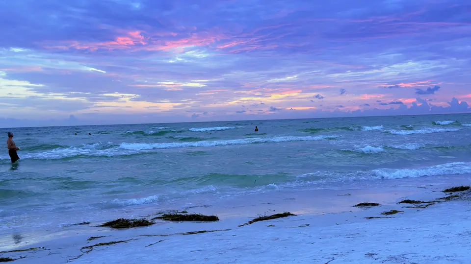 Pink and violet sunset clouds over rolling Gulf surf on Lido Key beach