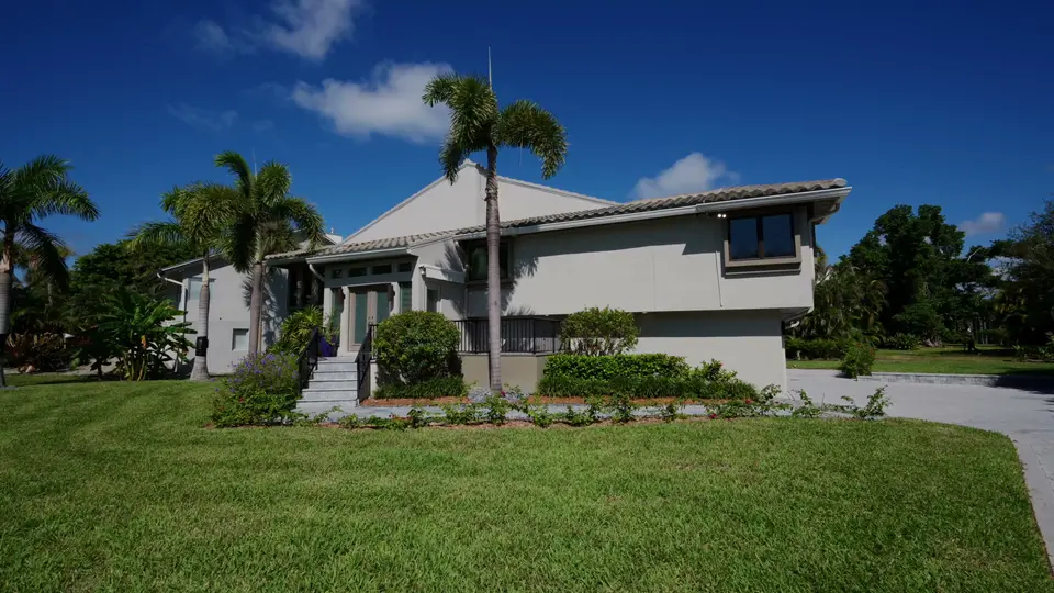 Two-story home with tile roof, palms and a green lawn under a deep blue sky