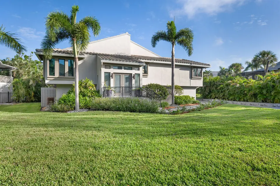 Light gray home with tall palms, tropical landscaping and a wide lawn