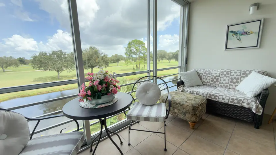 Glass-enclosed sunroom with bistro seating overlooking a golf course and pond