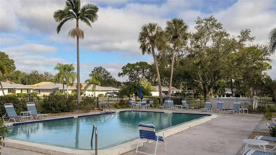 Community pool with lounge chairs, palms and oaks under a partly cloudy sky