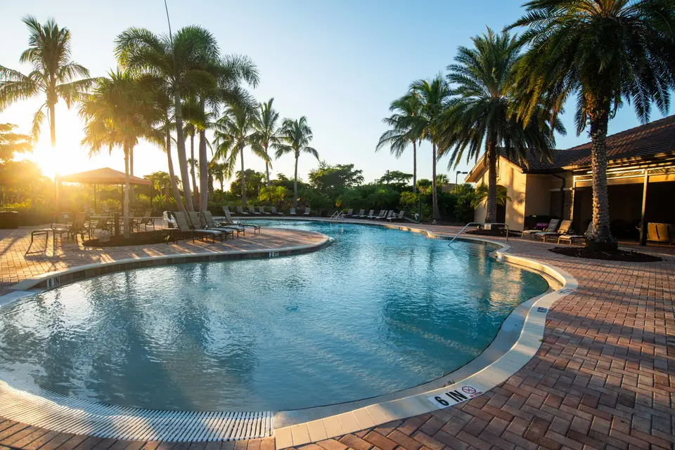 Resort-style community pool with brick pavers and palms at sunset