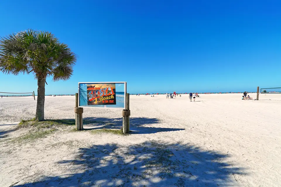 Siesta Beach sign and palm tree on wide white sand with the Gulf beyond