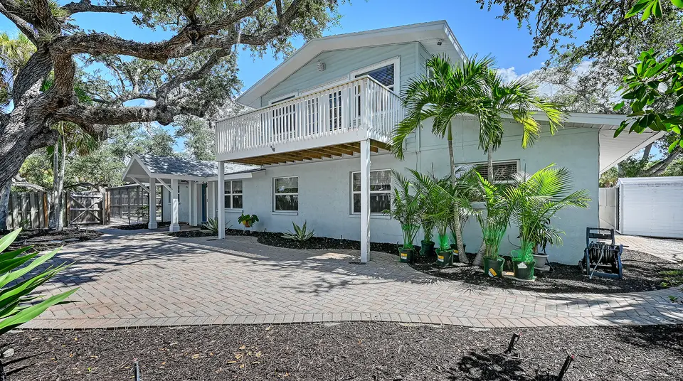 Two-story coastal home with an upper balcony, paver drive and live oak canopy
