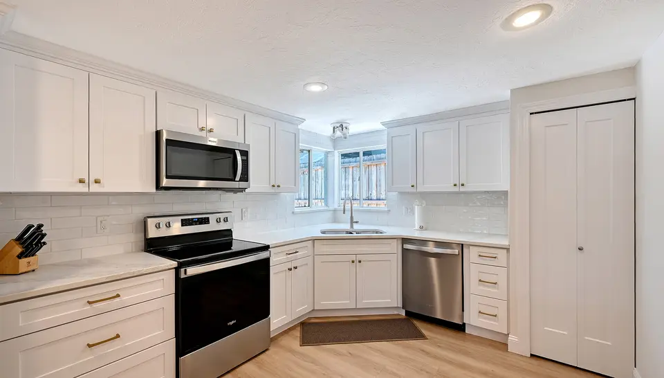 White kitchen with stainless appliances, quartz counters and light wood floors