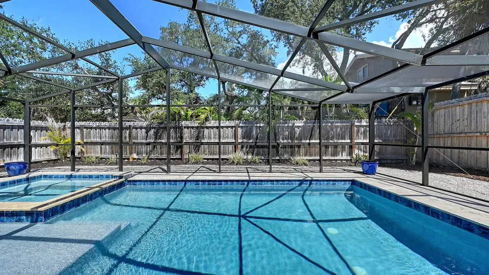 Screened pool and spa with a travertine deck framed by mature oaks
