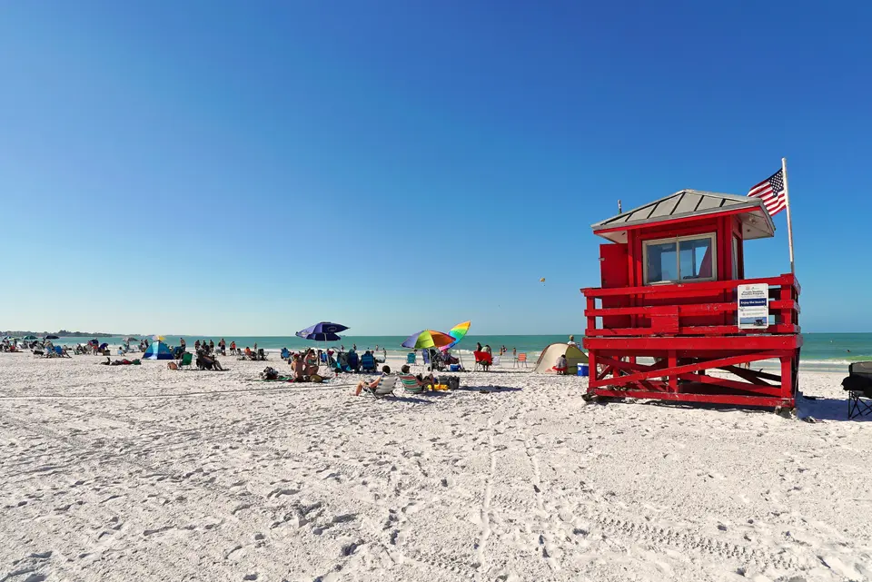 Red lifeguard stand on the white sand of Siesta Beach under a clear blue sky