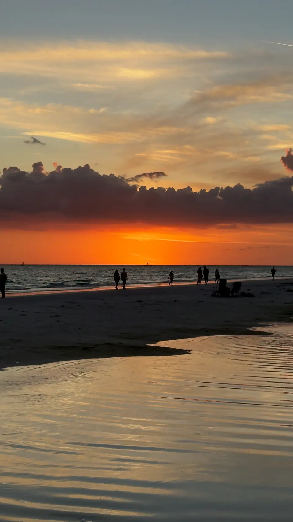 Orange sunset under dark clouds reflected in wet sand at the Siesta Key shoreline
